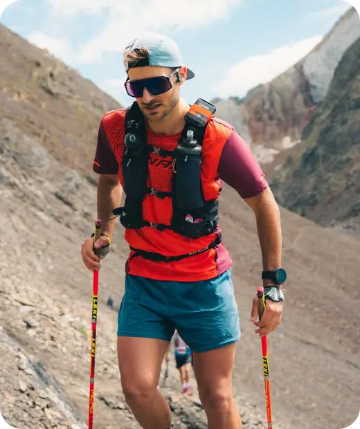 A trail runner with poles climbs a mountain path during a race